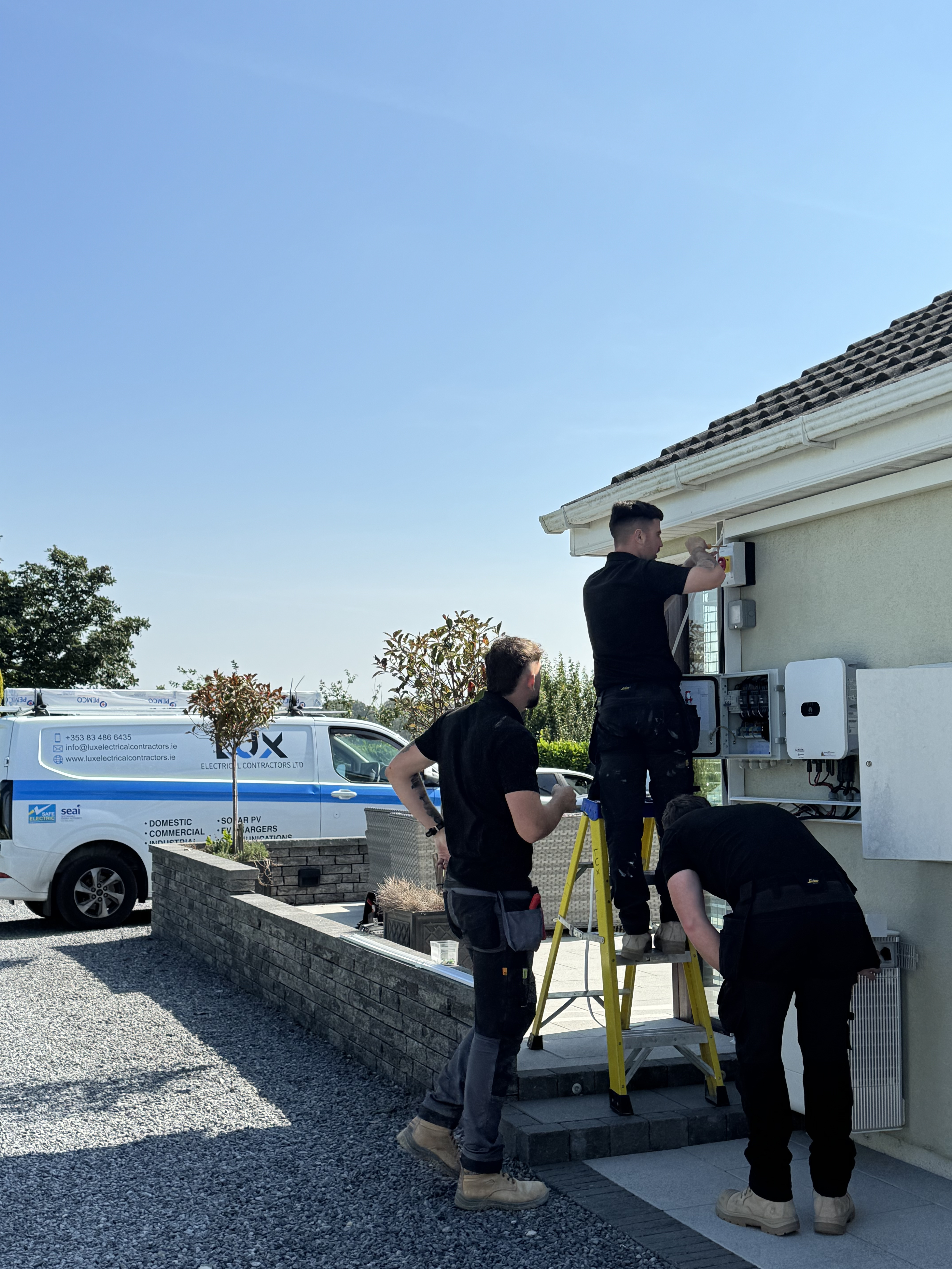 Lux team installing a solar inverter and switchgear on a home exterior